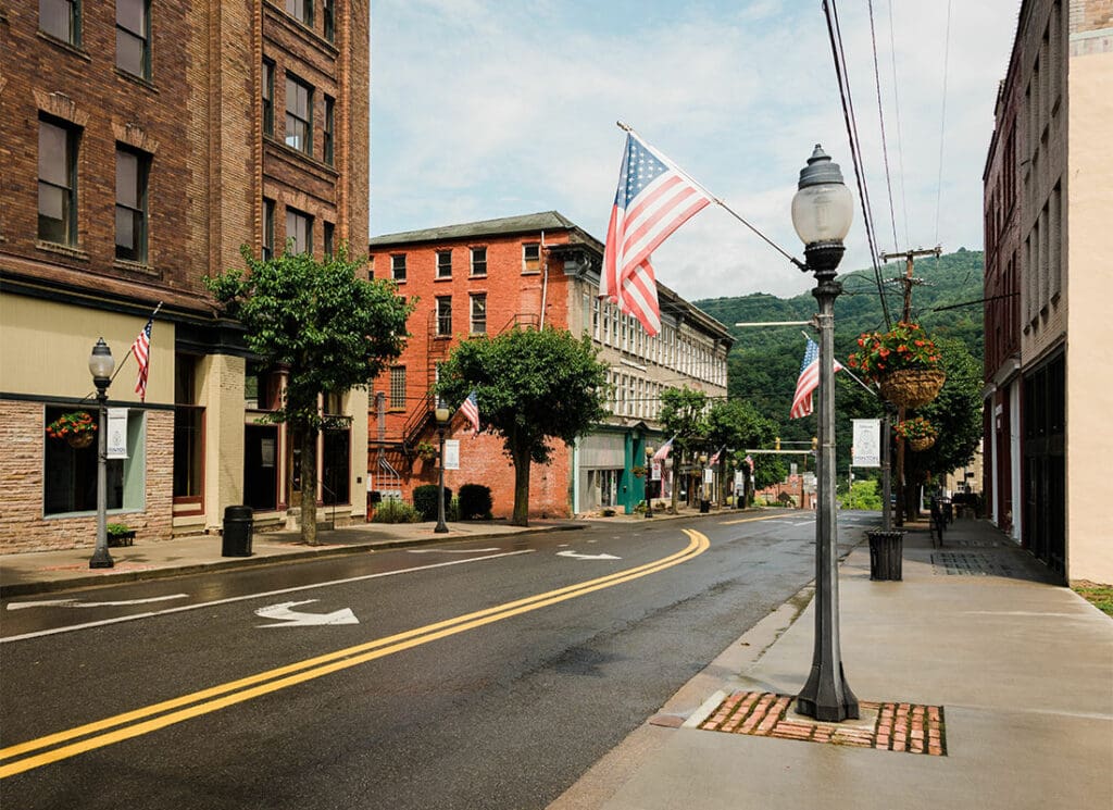 About Our Agency - View of Commercial Buildings Along a Main Street in a City in West Virginia with American Flags on the Lamp Posts