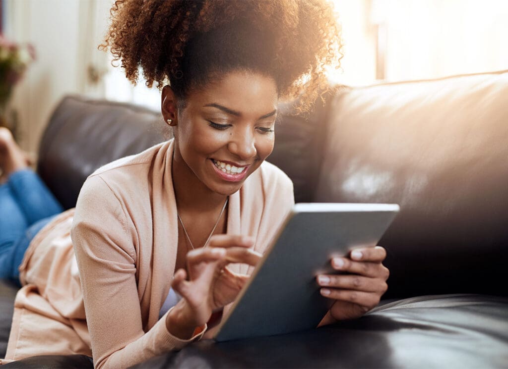 Blog - Closeup View of a Smiling Young Woman Laying on the Sofa While Reading on a Tablet at Home