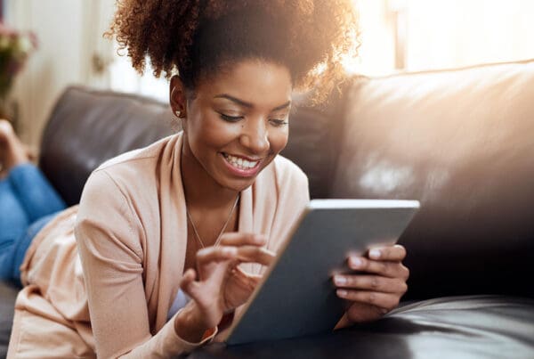 Blog - Closeup View of a Smiling Young Woman Laying on the Sofa While Reading on a Tablet at Home