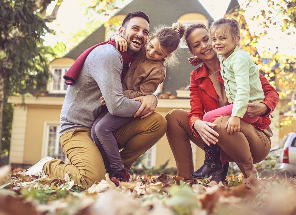 Personal Insurance - Portrait of Cheerful Parents Having Fun Holding and Playing with Their Two Daughters in the Backyard During the Fall